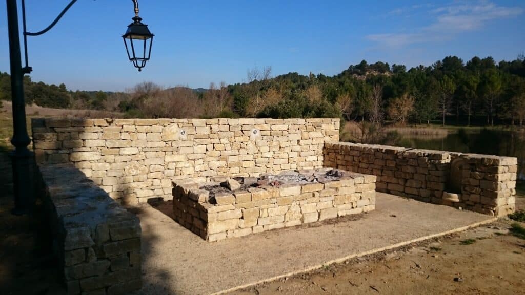 Barbecue extérieur en pierre sèche avec murs de soutènement et lanterne vintage dans un jardin paysager.