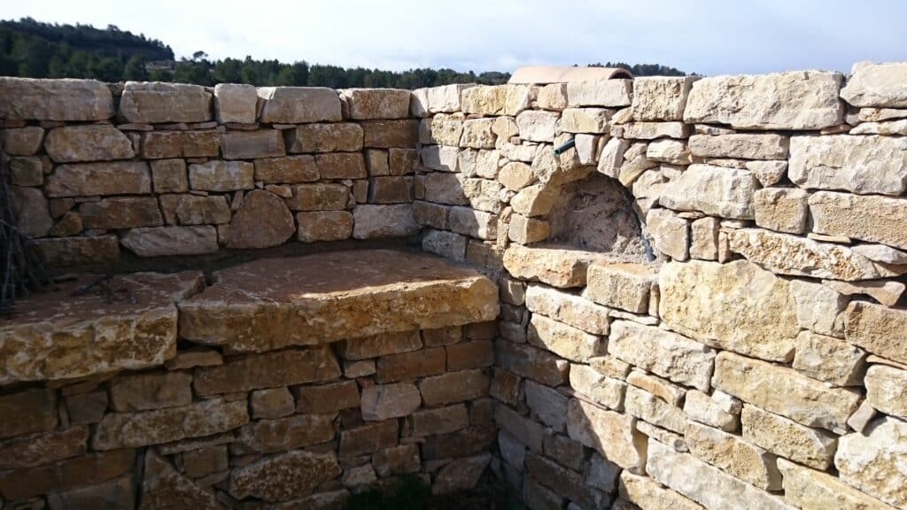 Mur en pierres sèches avec banc intégré et niche cintrée, maçonnerie traditionnelle en extérieur.