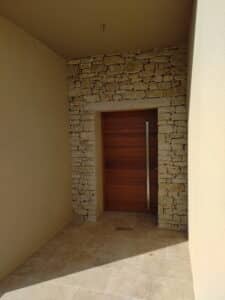 Porte bois moderne, poignée inox, mur pierres sèches et sol en travertin.