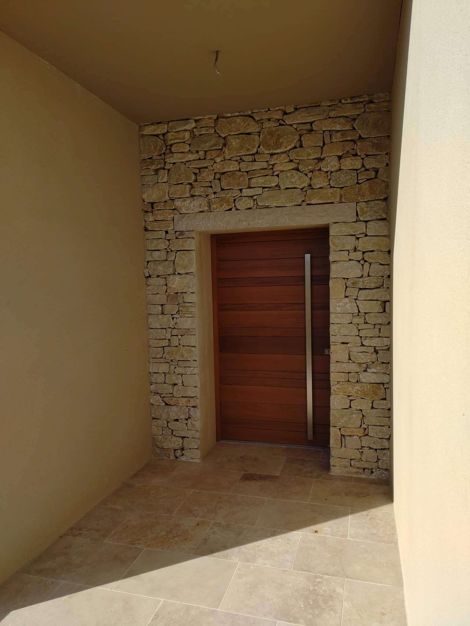 Porte bois moderne, poignée inox, mur pierres sèches et sol en travertin.