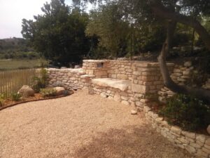 Banc et muret en pierre sèche dans un jardin paysager avec gravier et végétation méditerranéenne.