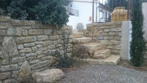 Mur de soutènement et escalier en pierre naturelle dans un jardin paysager avec plantes méditerranéennes.